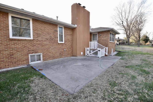 rear view of property featuring a patio area, brick siding, a yard, and a chimney