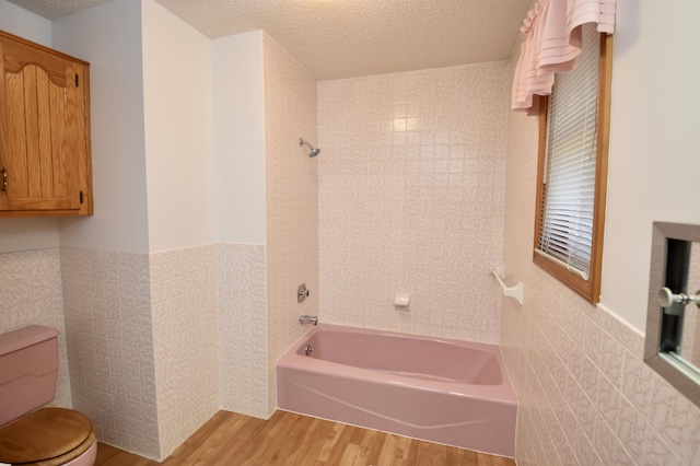 bathroom featuring toilet, wood finished floors, a textured ceiling, washtub / shower combination, and tile walls