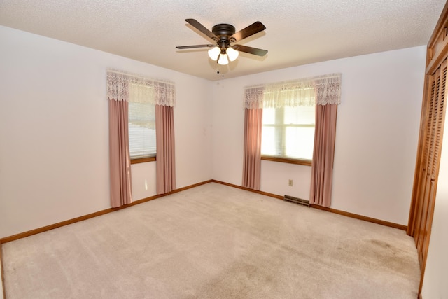 unfurnished room with light colored carpet, visible vents, ceiling fan, a textured ceiling, and baseboards