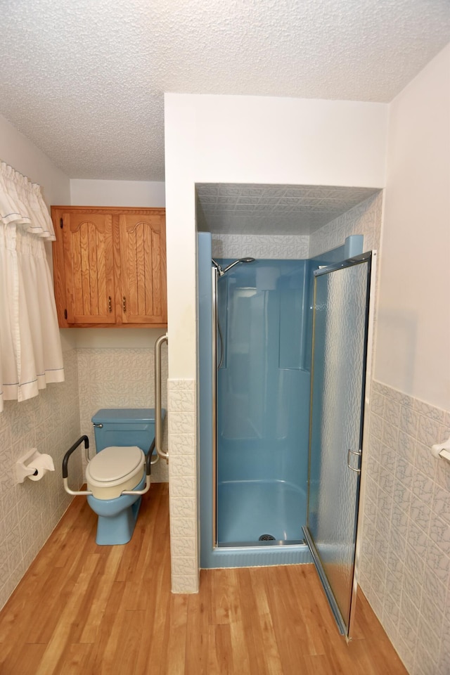 bathroom with a textured ceiling, wainscoting, wood finished floors, and a shower stall