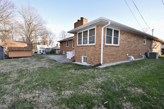 view of side of property featuring a lawn, a chimney, an outbuilding, a storage unit, and brick siding