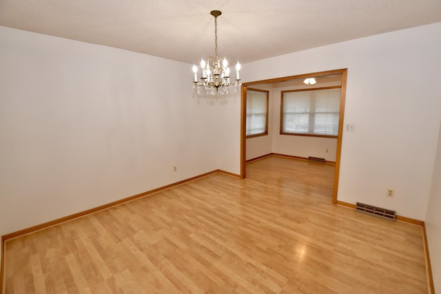 empty room with light wood-type flooring, baseboards, visible vents, and a textured ceiling