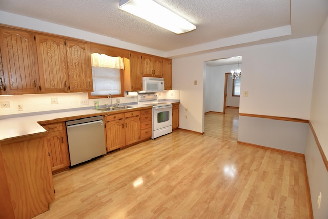 kitchen featuring white appliances, a sink, a textured ceiling, and light wood finished floors