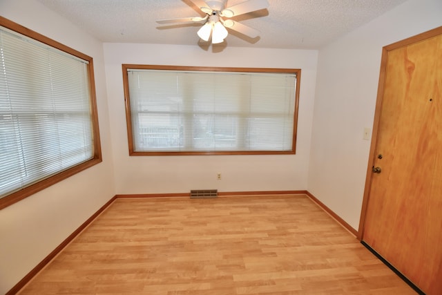 spare room featuring baseboards, light wood-style flooring, visible vents, and a textured ceiling