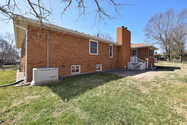 rear view of property with brick siding, a yard, a chimney, and fence