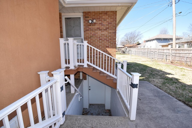 entrance to property featuring brick siding, fence, and a lawn