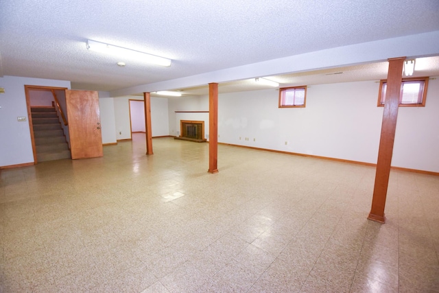 below grade area with a textured ceiling, a fireplace, baseboards, stairs, and light floors