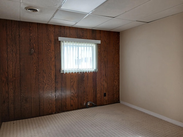 spare room featuring light carpet, a drop ceiling, and wood walls