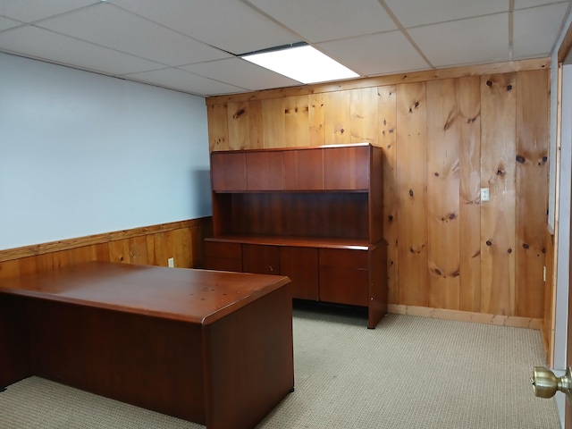 unfurnished office featuring light colored carpet, a drop ceiling, and wood walls