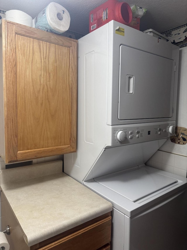 washroom with stacked washer and dryer, cabinets, and a textured ceiling