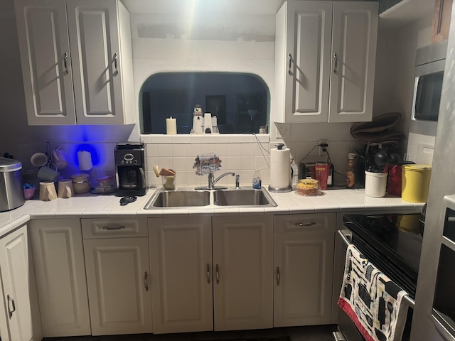 kitchen with tasteful backsplash, sink, appliances with stainless steel finishes, tile counters, and white cabinets