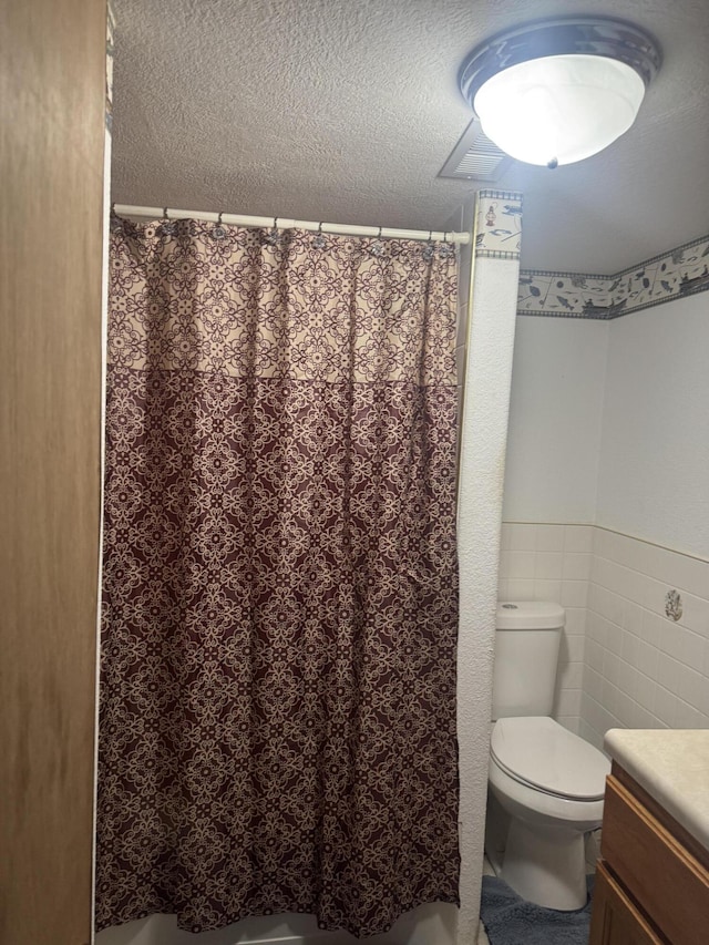 bathroom featuring tile walls, toilet, vanity, and a textured ceiling