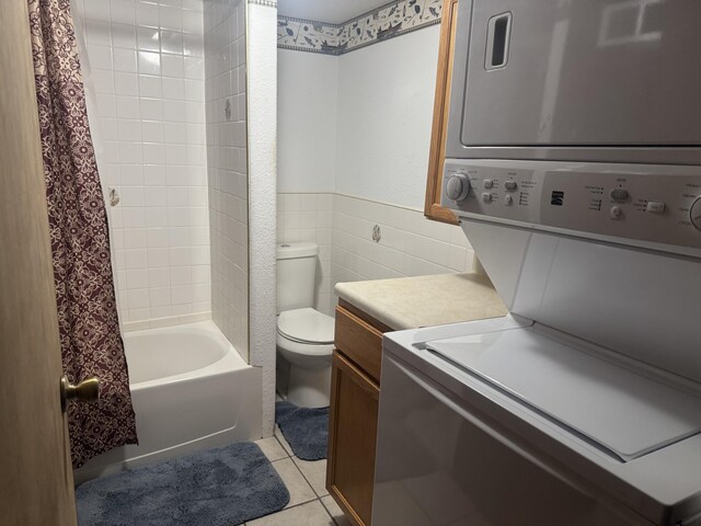 full bathroom with toilet, stacked washer and clothes dryer, tile patterned flooring, tile walls, and vanity