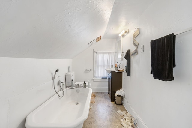 bathroom with a textured ceiling, vanity, a tub, toilet, and vaulted ceiling