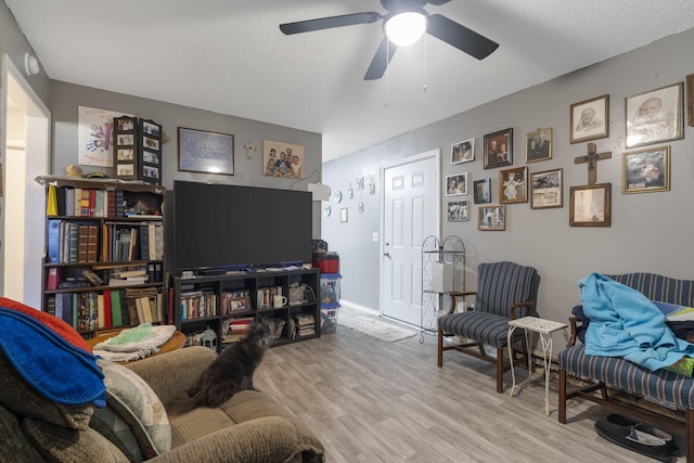 living room with a textured ceiling, ceiling fan, and light hardwood / wood-style flooring