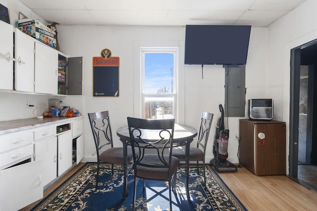 dining room featuring light wood-type flooring, a paneled ceiling, and electric panel