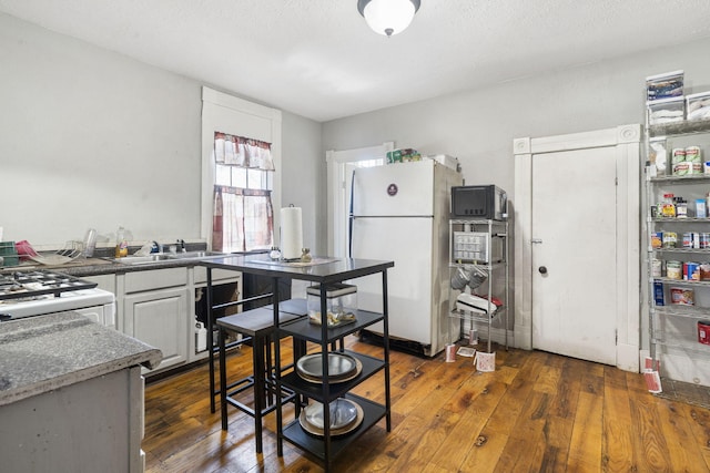 kitchen with white appliances, a textured ceiling, dark wood-type flooring, dark stone counters, and sink