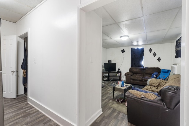 living room featuring a drop ceiling, dark wood-type flooring, and a wall mounted air conditioner