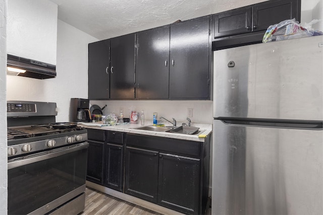 kitchen featuring light wood-type flooring, appliances with stainless steel finishes, a textured ceiling, and sink