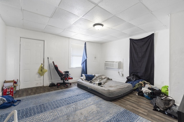 bedroom with hardwood / wood-style floors, a wall mounted AC, and a drop ceiling