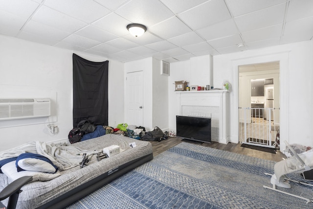 living room with a wall mounted AC, a drop ceiling, dark hardwood / wood-style floors, and a brick fireplace