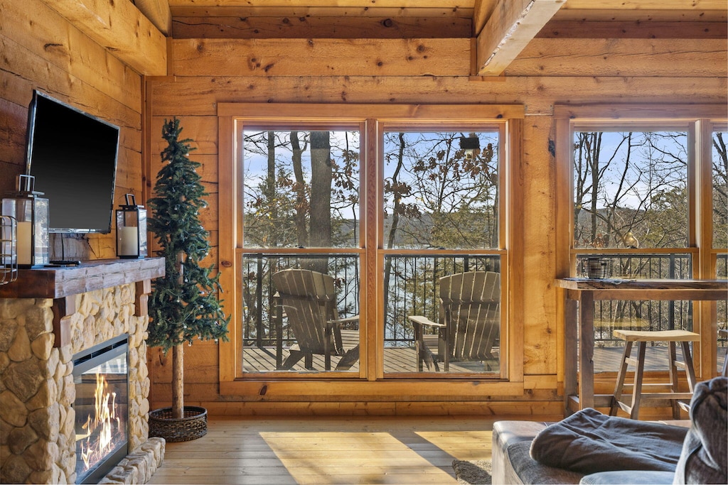 living room with wood-type flooring, beamed ceiling, and a stone fireplace