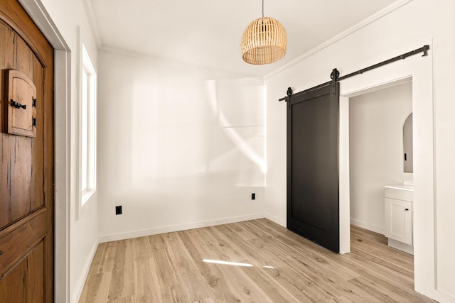 unfurnished bedroom featuring light wood-type flooring, ensuite bathroom, crown molding, and a barn door