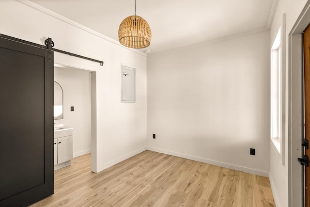 unfurnished bedroom featuring a barn door, light wood-type flooring, and ornamental molding