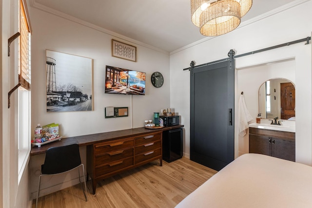 bedroom with a barn door, sink, an inviting chandelier, light hardwood / wood-style flooring, and ornamental molding