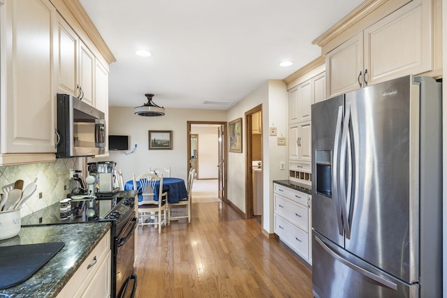 kitchen with tasteful backsplash, hardwood / wood-style flooring, appliances with stainless steel finishes, dark stone counters, and cream cabinets