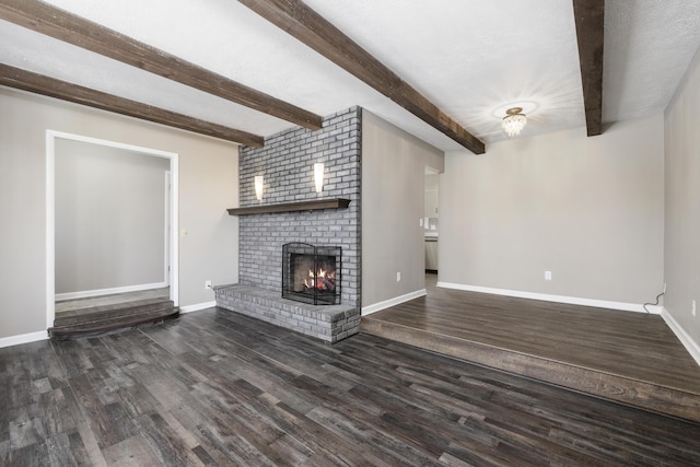 unfurnished living room featuring dark hardwood / wood-style flooring, beamed ceiling, a textured ceiling, and a brick fireplace