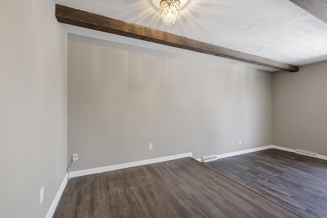 empty room featuring a textured ceiling, dark wood-type flooring, and beamed ceiling