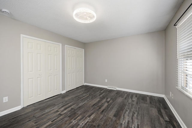 unfurnished bedroom with dark hardwood / wood-style floors, a textured ceiling, and two closets