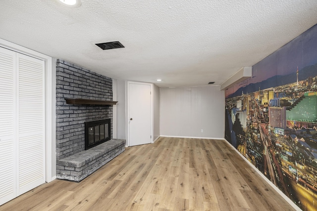 unfurnished living room featuring a brick fireplace, a textured ceiling, and light hardwood / wood-style floors