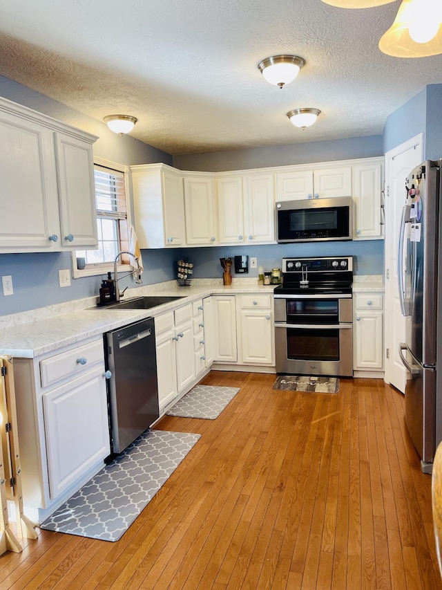 kitchen with a textured ceiling, appliances with stainless steel finishes, light hardwood / wood-style floors, and white cabinets