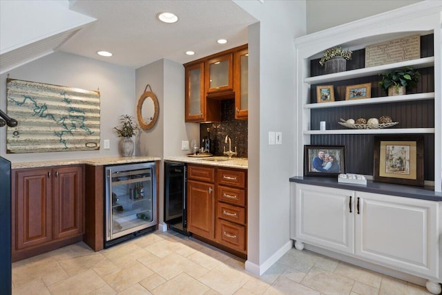 bar featuring light stone countertops, decorative backsplash, beverage cooler, and sink