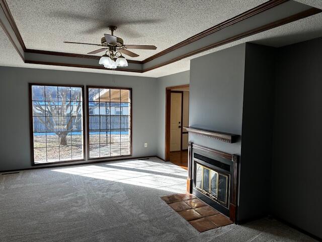 unfurnished living room with ceiling fan, carpet flooring, ornamental molding, and a raised ceiling