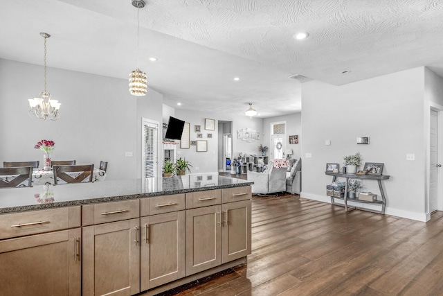 kitchen featuring a textured ceiling, dark stone counters, an inviting chandelier, hanging light fixtures, and dark hardwood / wood-style floors