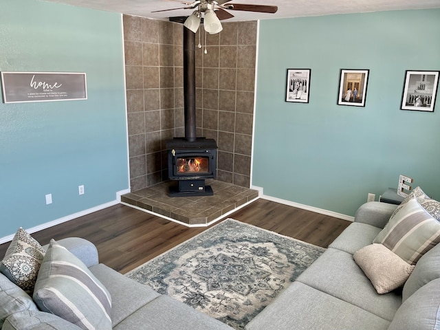 living room with ceiling fan, a wood stove, and wood-type flooring