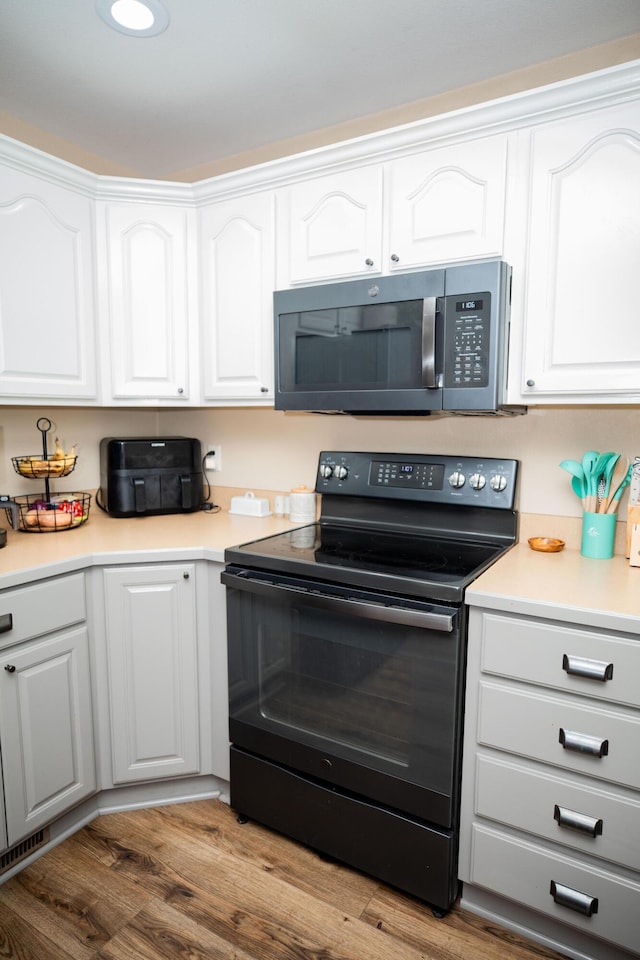 kitchen with wood-type flooring, white cabinets, and black electric range oven