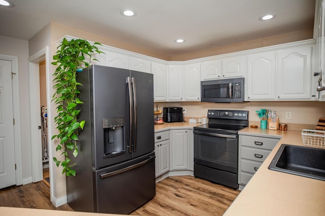 kitchen with white cabinets, appliances with stainless steel finishes, light hardwood / wood-style flooring, and sink