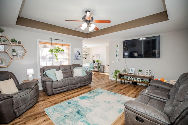 living room with a raised ceiling, ceiling fan, and hardwood / wood-style flooring