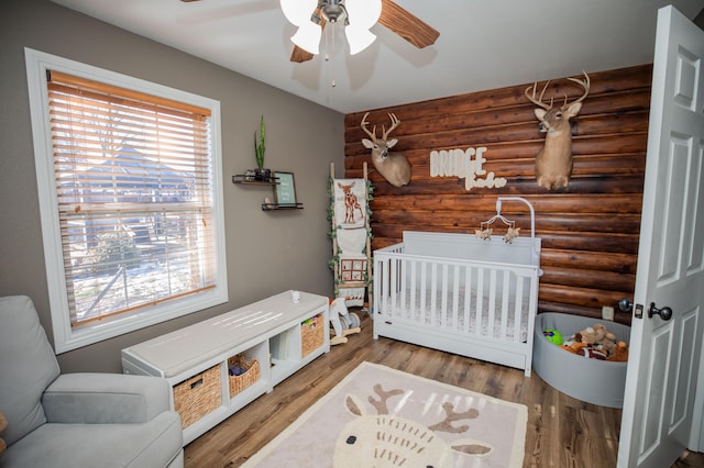 bedroom with ceiling fan, hardwood / wood-style flooring, rustic walls, and a crib