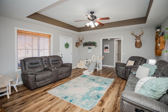 living room with ceiling fan, a tray ceiling, and hardwood / wood-style flooring