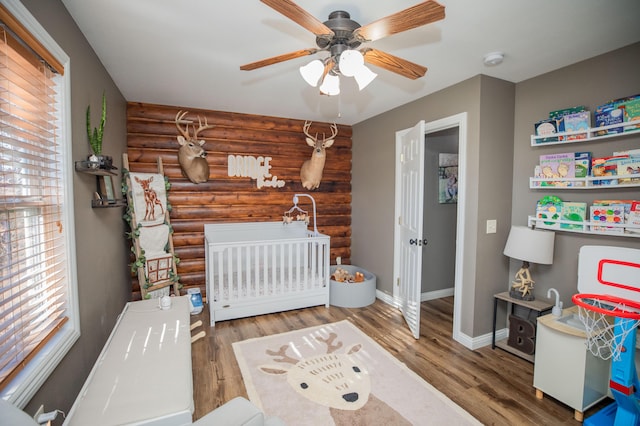 bedroom with ceiling fan, hardwood / wood-style flooring, rustic walls, and a crib