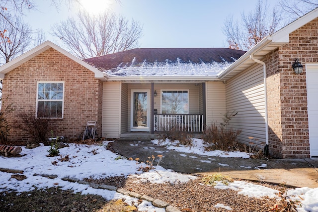 snow covered property entrance featuring covered porch and a garage