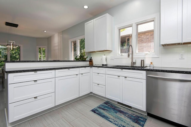 kitchen featuring stainless steel dishwasher, sink, dark stone countertops, and white cabinetry