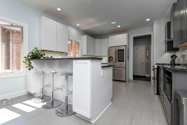 kitchen featuring kitchen peninsula, a breakfast bar area, appliances with stainless steel finishes, dark stone counters, and white cabinets