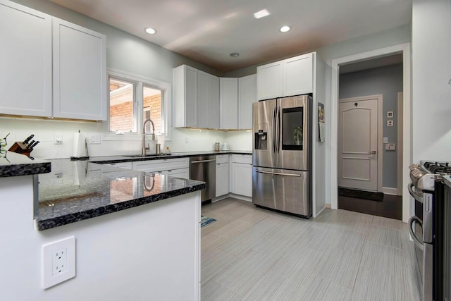 kitchen featuring white cabinets, appliances with stainless steel finishes, dark stone counters, sink, and kitchen peninsula