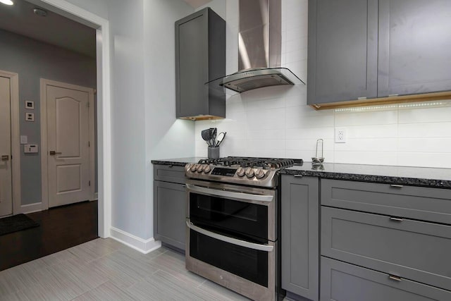 kitchen with wall chimney exhaust hood, tasteful backsplash, dark stone countertops, double oven range, and gray cabinetry